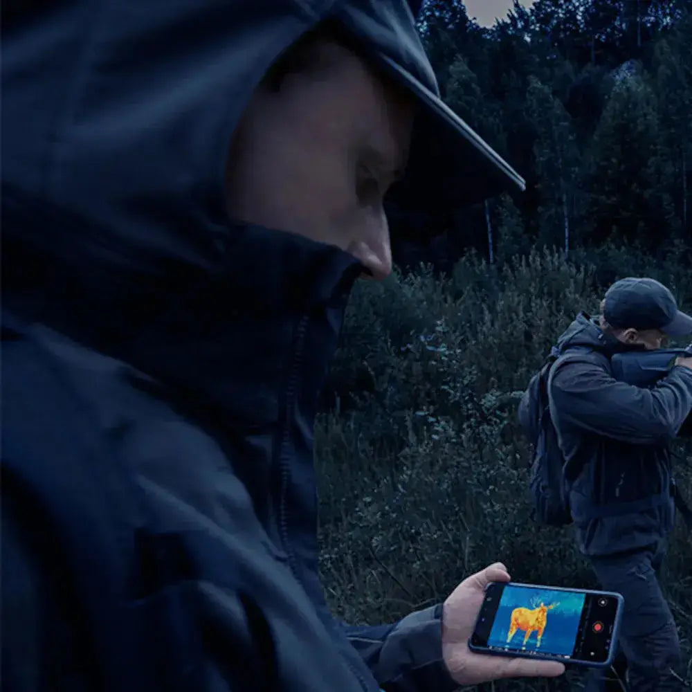 Hunter using Pulsar Thermion2 XL60 LRF thermal scope with smartphone thermal imaging display in outdoor forest environment.