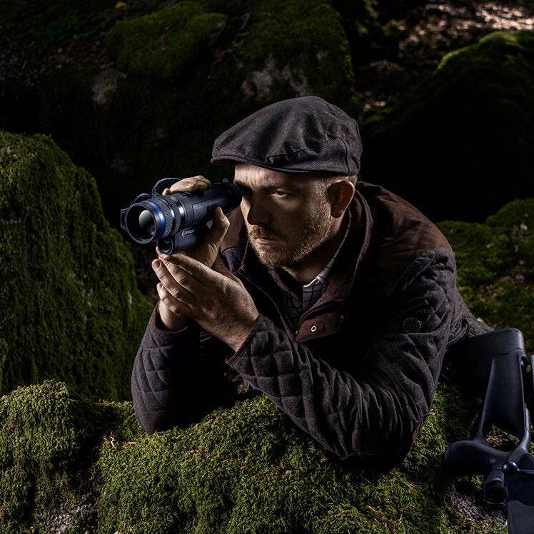 Man aiming Pulsar Telos XP50 thermal monocular in mossy forest, emphasizing precision optics and outdoor performance.