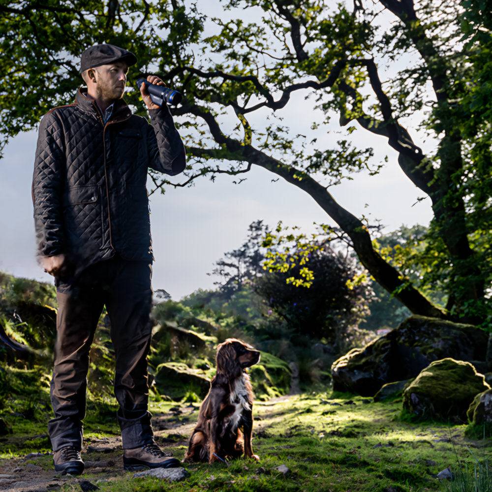Hunter with dog using Pulsar Telos XG50 thermal monocular in forest, emphasizing its upgradeable features and outdoor performance.