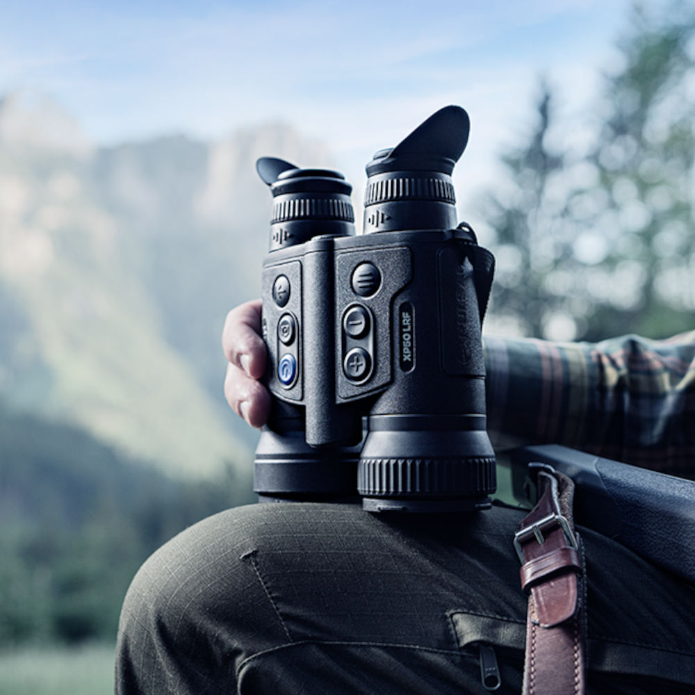 Close-up of Pulsar Merger XP35 LRF thermal binoculars resting on a knee, showing control panel and eyepieces. Built for high-performance optics use.