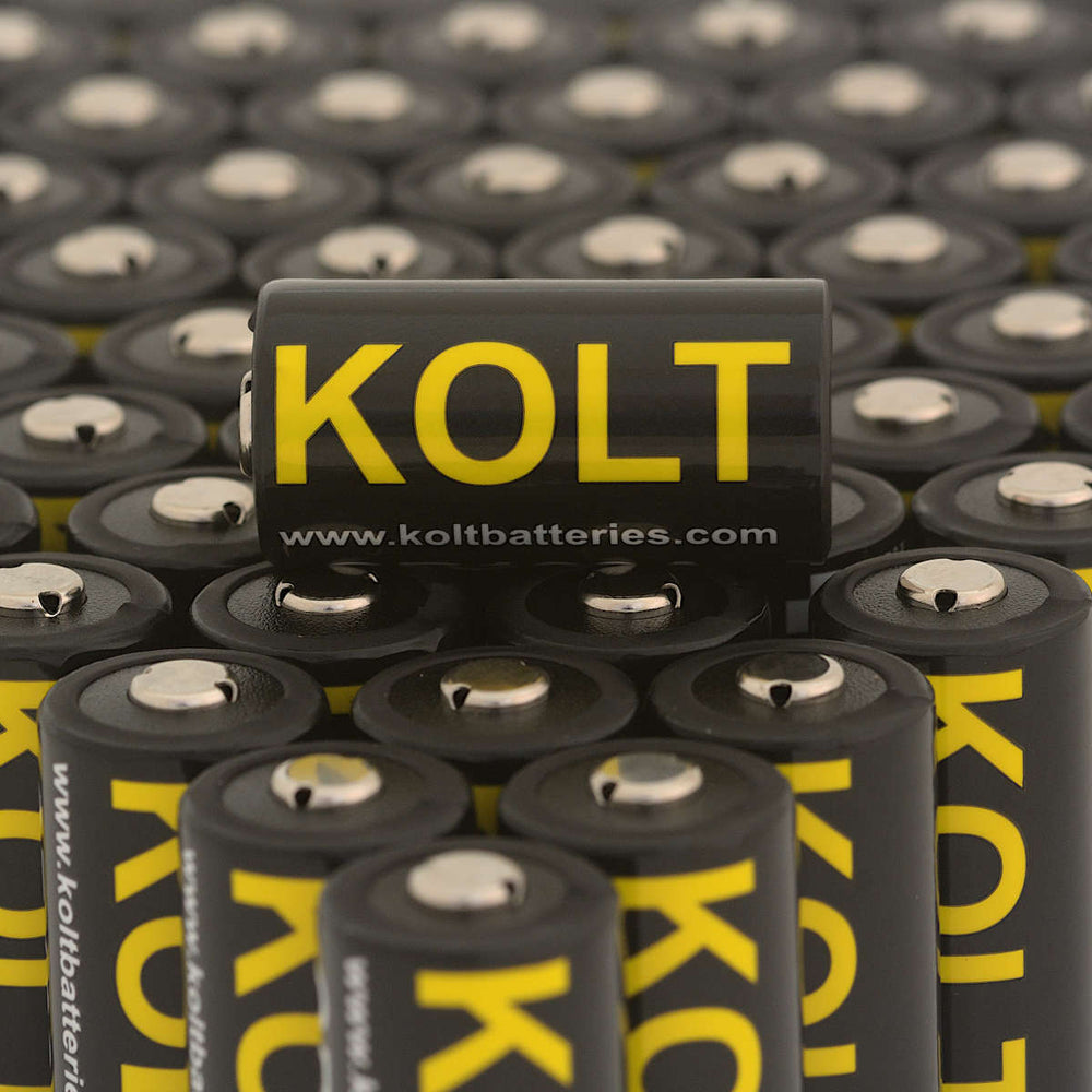 Kolt CR123A battery with bold yellow logo on black casing, placed among multiple units. High-performance disposable battery for tactical devices.