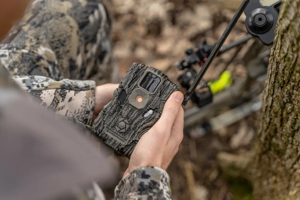 Hunter holding Stealthcam Fusion Trail Camera in the field, showcasing its compact design and easy setup for remote wildlife tracking.